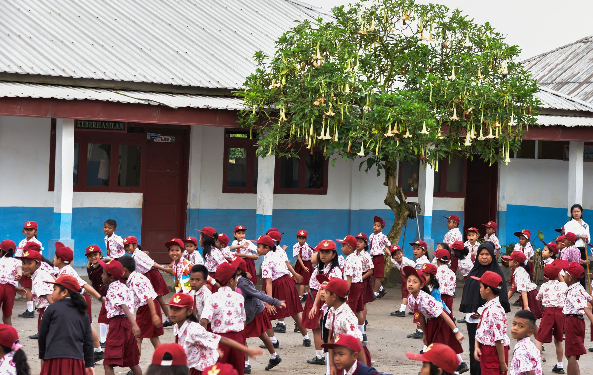 Students in maroon uniforms are morning exercises outside the school (Sumatra, Indonesia)